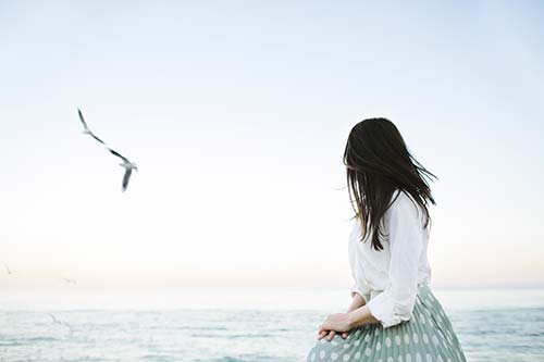 a woman sitting on the beach looking at a bird