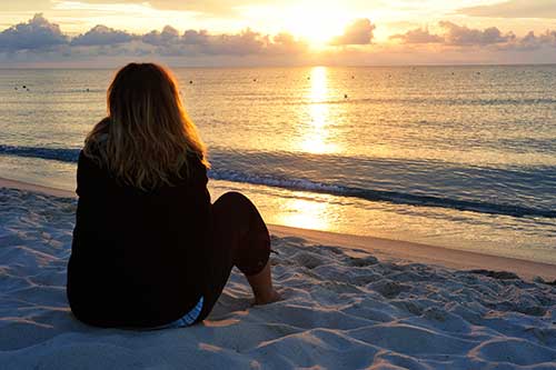 a woman sitting on a beach looking at the sunset