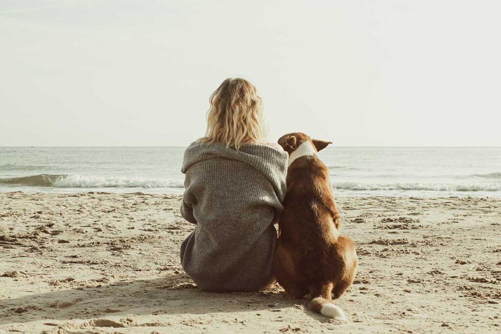 a woman and dog sitting on a beach
