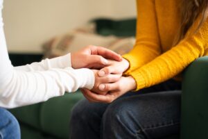 Close-up of two people sitting together, one gently holding the other's hands in a comforting gesture.