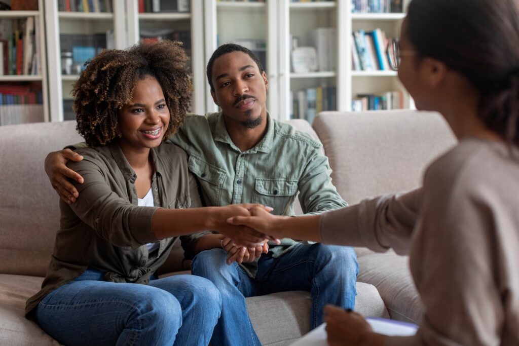 A smiling couple shakes hands with a therapist during a counseling session.
