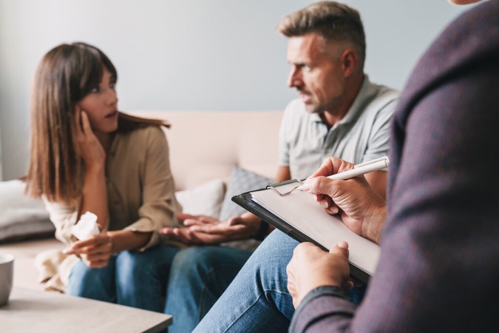 A couple speaks with a therapist, expressing concern during a counseling session.