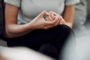 Close-up of a person sitting with hands clasped tightly in their lap, showing a gesture of anxiety or nervousness.