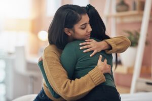 Two women hugging each other warmly indoors, conveying comfort and emotional support.