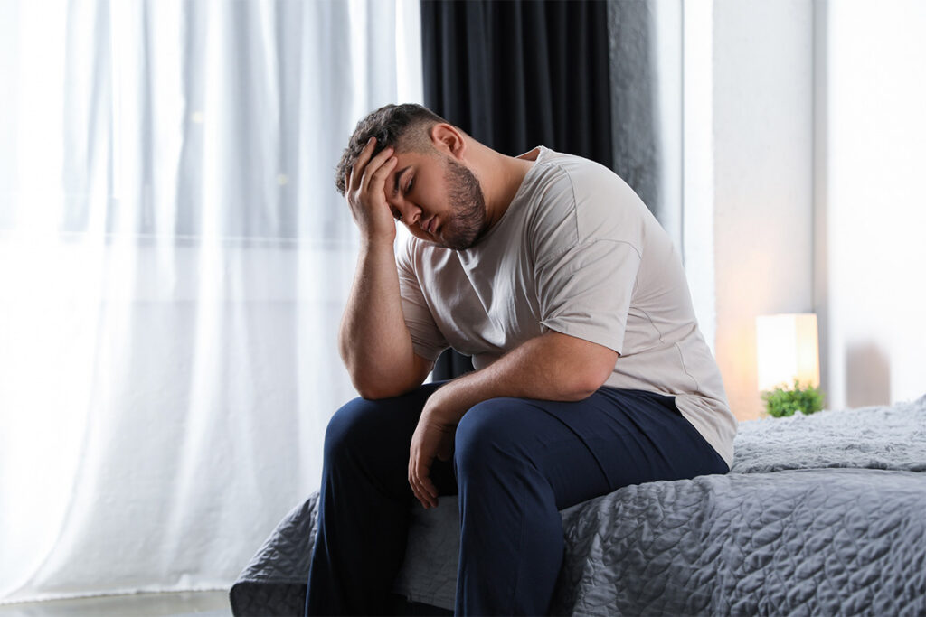 Man sitting at edge of bed with a headache