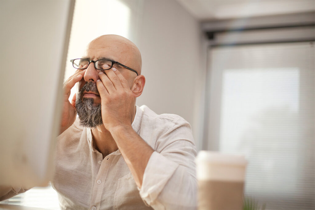 Man trying to use computer rubbing eyes